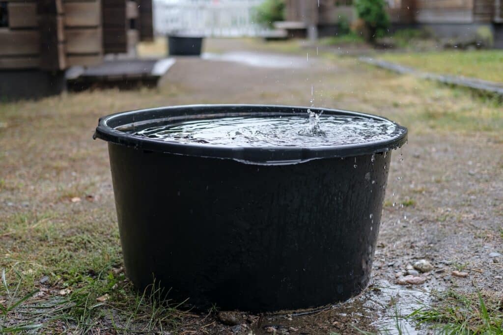 Das Regenwasser wird an einem Sommertag in einer Auffangwanne unter der Dachrinne im Hof gesammelt.