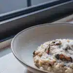 Cremiges Pilzrisotto mit gebräunten Champignons und geriebenem Parmesan in einer flachen Schale