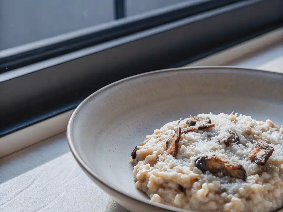 Cremiges Pilzrisotto mit gebräunten Champignons und geriebenem Parmesan in einer flachen Schale