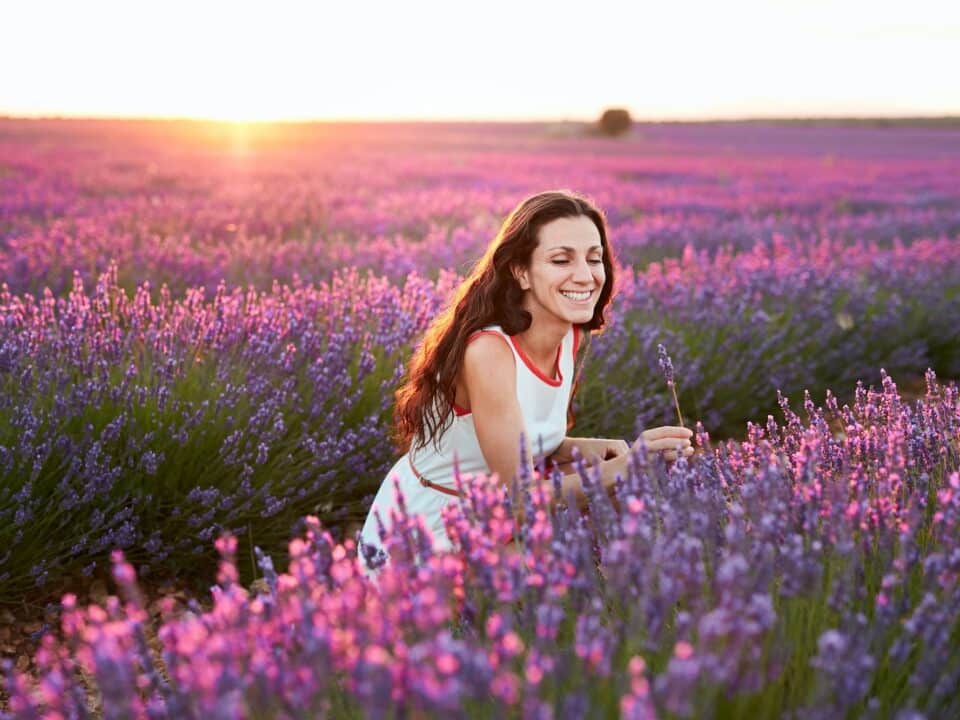 Woman standing between big violet lavender field at sunset